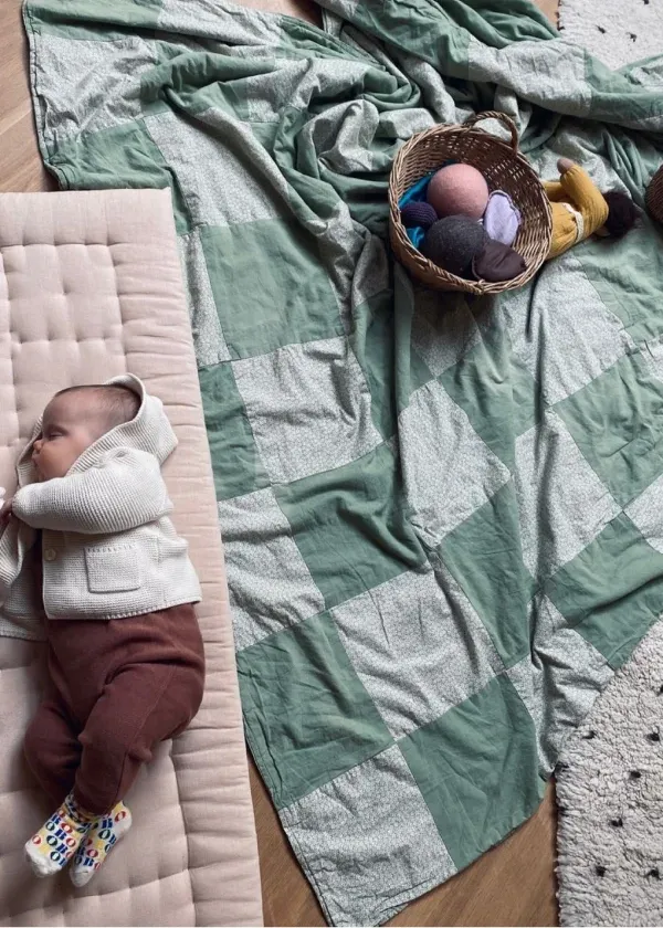 A baby peacefully sleeping in warm clothes on a cozy padded blanket, reflecting the gentle and nurturing atmosphere of our Pikler-inspired play group