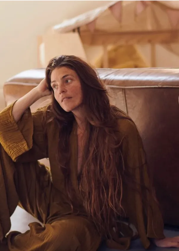 Bibi dressed with a earthy brown onesie, sitting on the floor and looking to the side