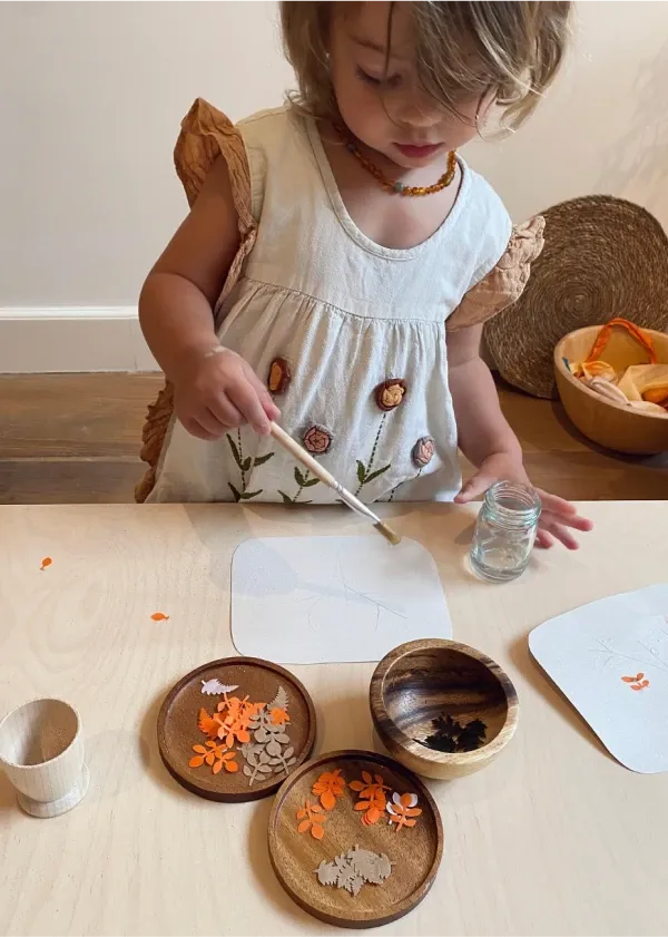 Little girl sticking orange and brown paper leaves on a card