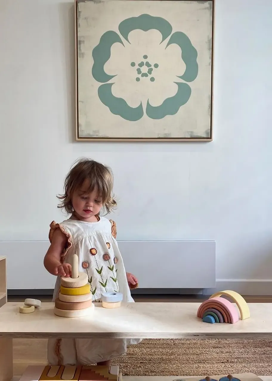 Girl playing with wooden stacking toys in front of a painting of a mallow flower