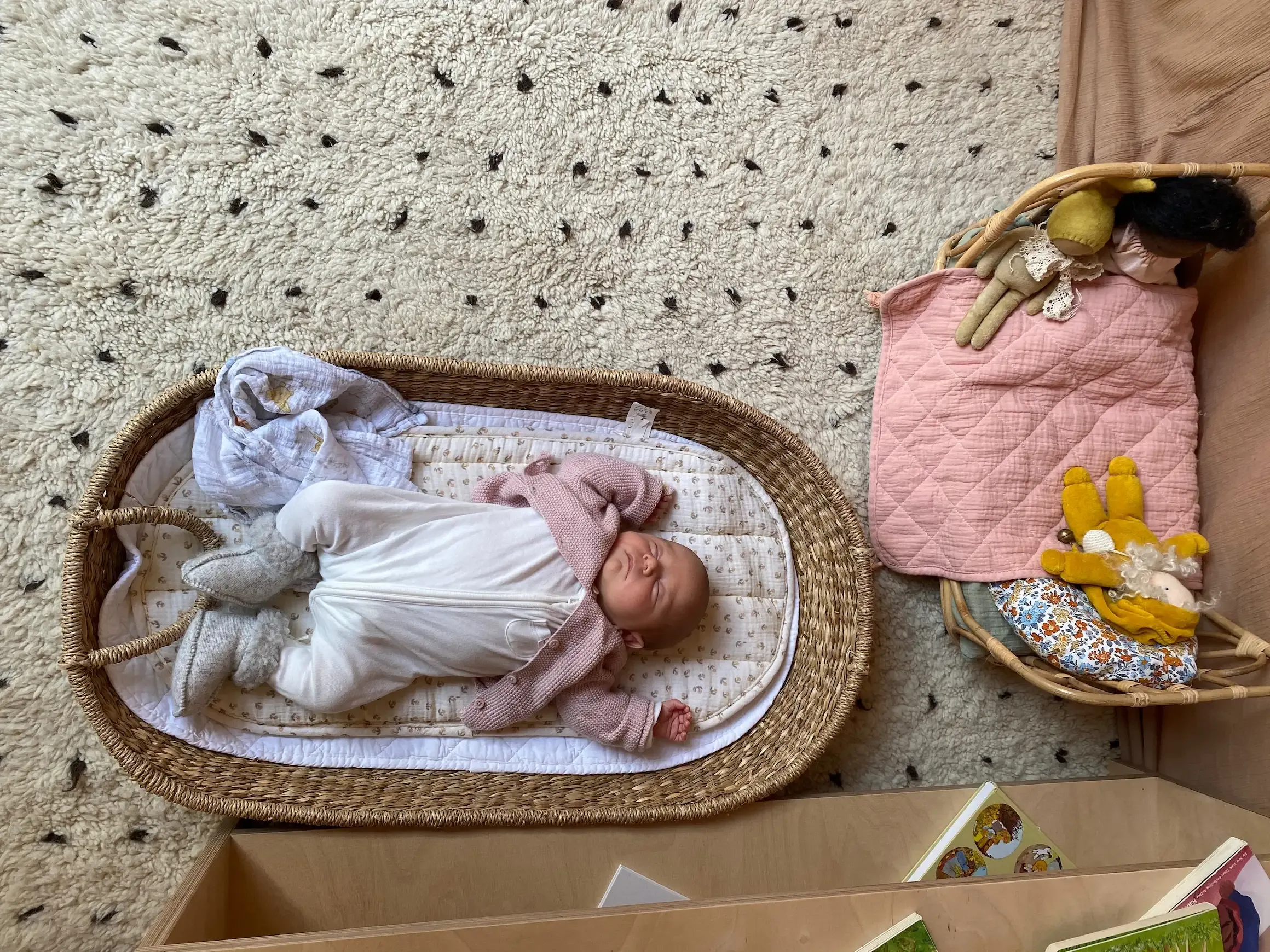 Baby sleeping peacefully inside a basket and wearing a knitted jacket